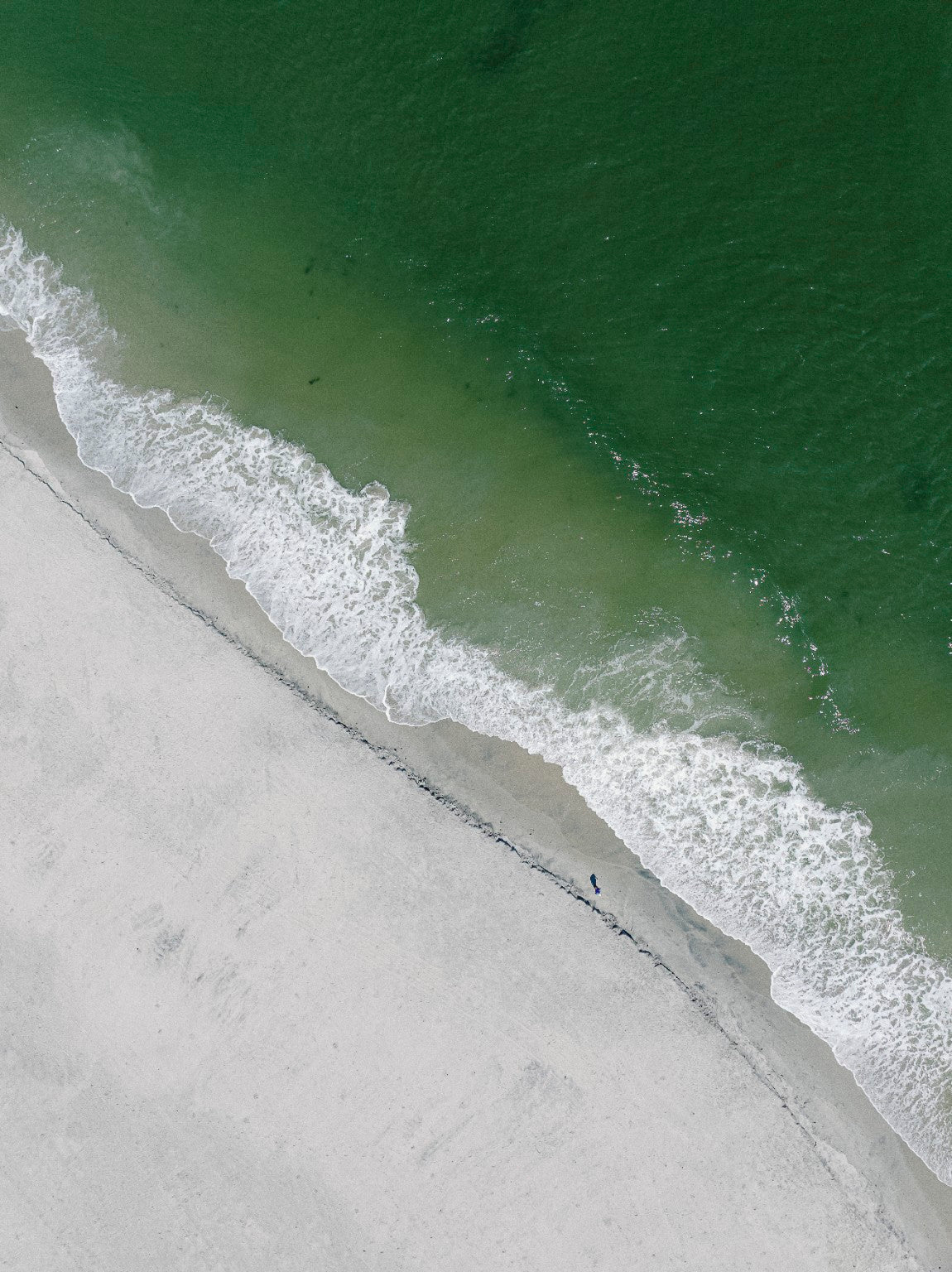 Aerial fine art photograph of emerald Atlantic water, white surf and a lone beachgoer on the South Jersey shore